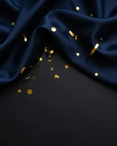 Goldenes Konfetti und Luftschlangen auf nachtblauer Seide