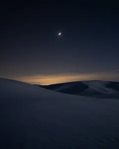 Mondsichel über verschneiten Hügeln unter einem Sternenhimmel