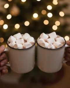 Zwei Tassen Kakao mit Marshmallows vor einer Lichterkette