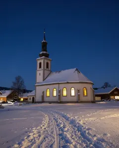 Verschneite Dorfkirche mit erleuchteten Fenstern bei Nacht